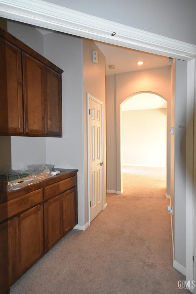 hall featuring light carpet, baseboards, and arched walkways