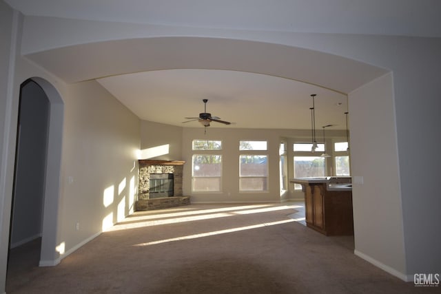 unfurnished living room featuring a healthy amount of sunlight, carpet, a fireplace, and arched walkways