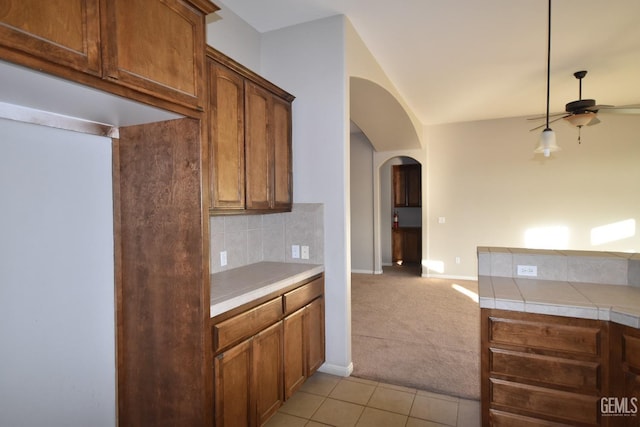 kitchen featuring arched walkways, light colored carpet, backsplash, a ceiling fan, and light tile patterned flooring