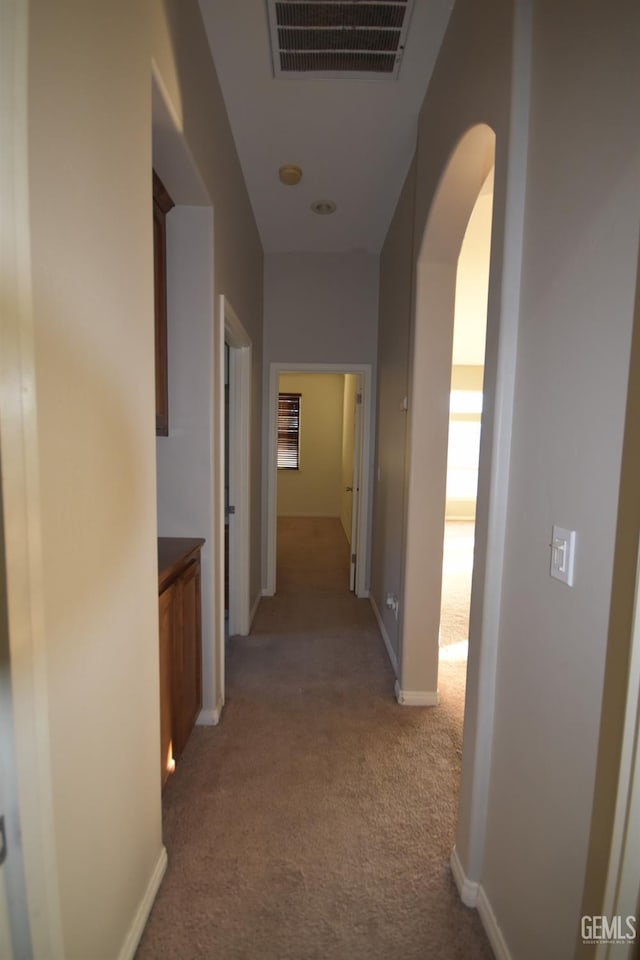 hallway with arched walkways, baseboards, visible vents, and light colored carpet