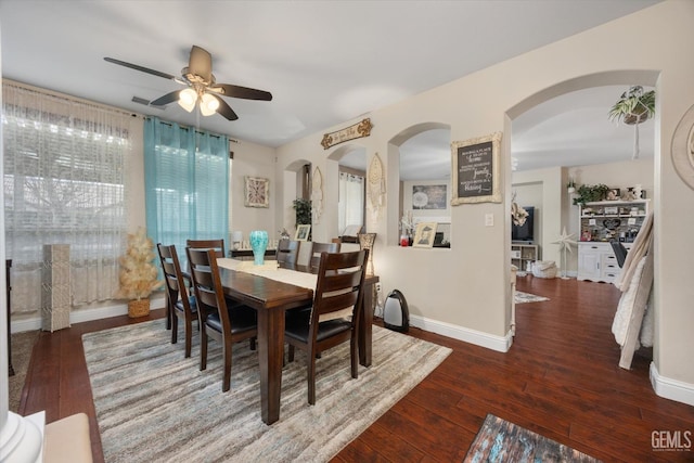 dining room featuring a ceiling fan, arched walkways, dark wood finished floors, and baseboards