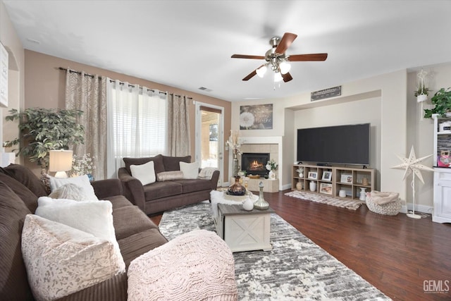 living area featuring baseboards, visible vents, dark wood finished floors, a tile fireplace, and ceiling fan