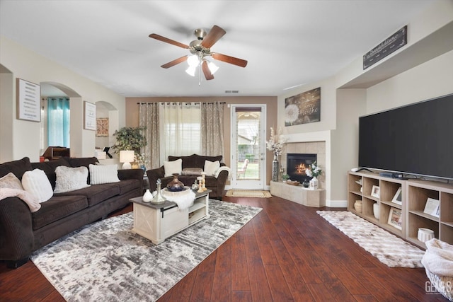 living area featuring dark wood-style floors, arched walkways, visible vents, ceiling fan, and a tile fireplace