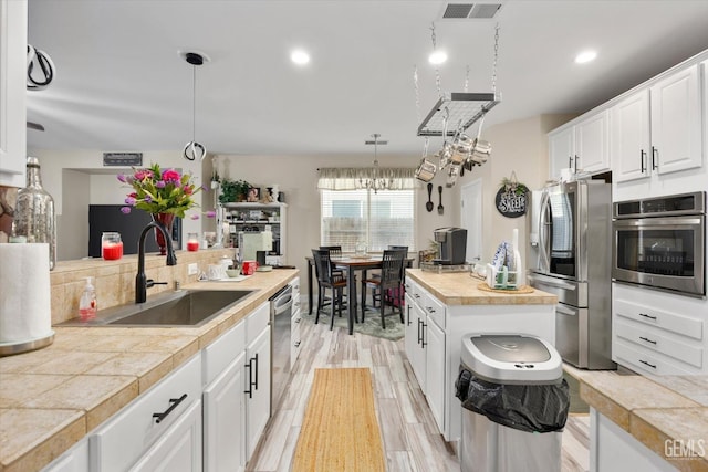 kitchen with decorative light fixtures, stainless steel appliances, visible vents, white cabinetry, and a sink