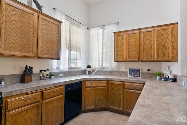 kitchen featuring brown cabinets, light countertops, black dishwasher, and a sink