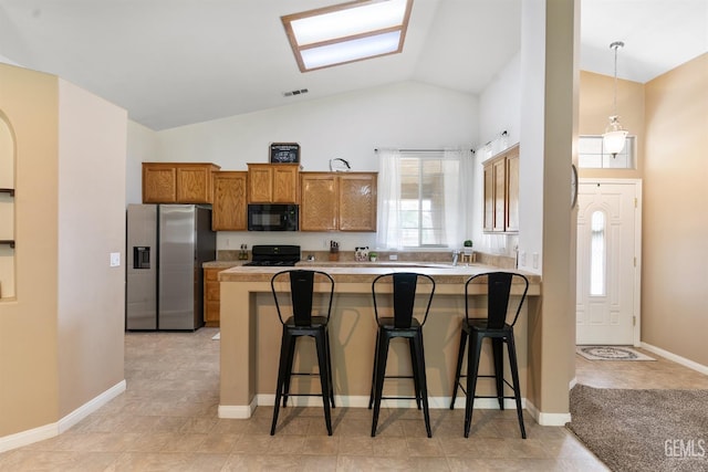 kitchen with visible vents, a kitchen bar, a peninsula, brown cabinetry, and black appliances