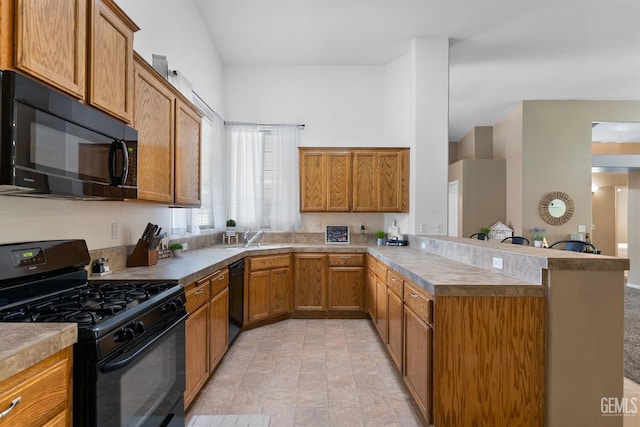 kitchen featuring black appliances, a sink, a peninsula, brown cabinetry, and light countertops