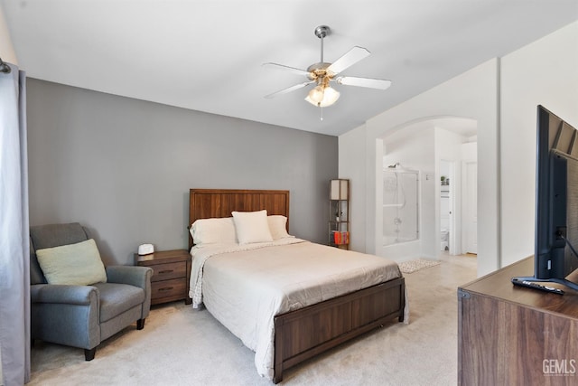 bedroom with a ceiling fan, arched walkways, ensuite bathroom, and light carpet