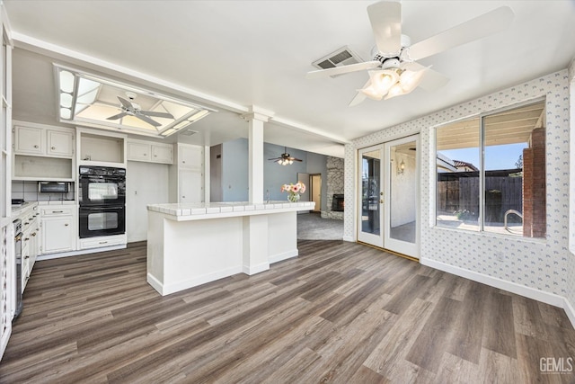 kitchen featuring white cabinetry, black double oven, tile countertops, a kitchen breakfast bar, and dark hardwood / wood-style flooring