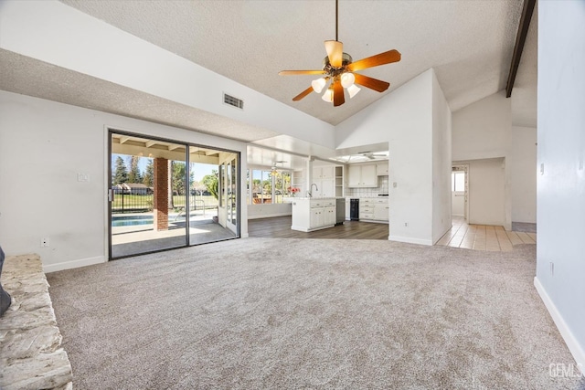 unfurnished living room with a textured ceiling, dark carpet, ceiling fan, beamed ceiling, and sink