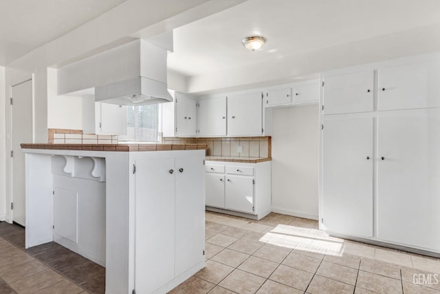 kitchen with kitchen peninsula, white cabinets, tasteful backsplash, light tile patterned floors, and tile countertops