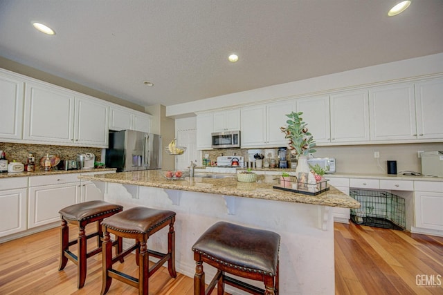 kitchen featuring white cabinets, a center island with sink, light hardwood / wood-style floors, light stone counters, and stainless steel appliances