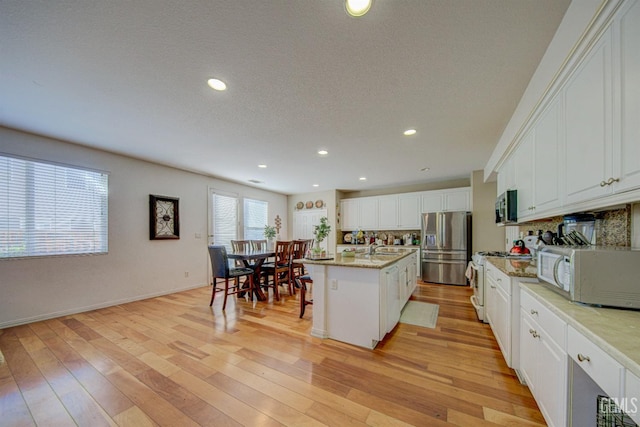 kitchen featuring decorative backsplash, white cabinetry, a kitchen island with sink, and appliances with stainless steel finishes