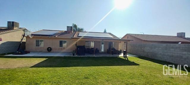 rear view of house with a patio area, a lawn, and solar panels