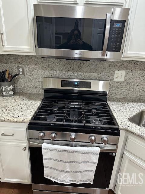 kitchen featuring tasteful backsplash, light stone countertops, white cabinetry, and stainless steel appliances