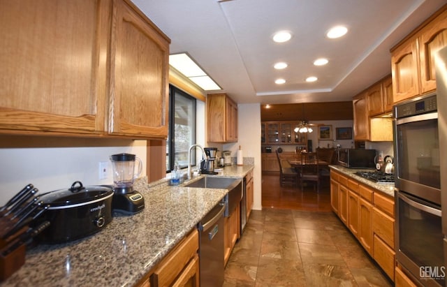 kitchen featuring light stone countertops, stainless steel appliances, a raised ceiling, sink, and hanging light fixtures