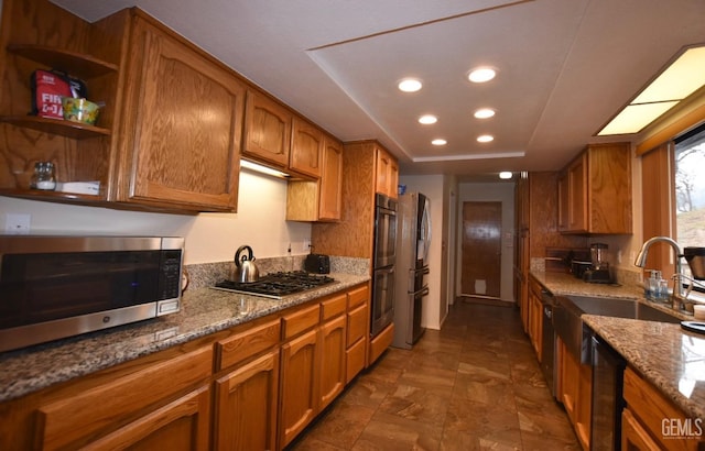 kitchen with sink, light stone counters, stainless steel appliances, and a tray ceiling