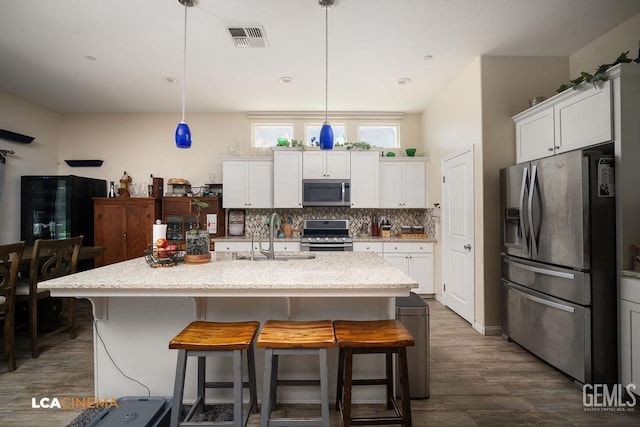 9311 Caliente Creek Ct, Bakersfield, CA 93311 - kitchen featuring stainless steel appliances, dark wood finished floors, white cabinets, a kitchen breakfast bar, and light stone countertops