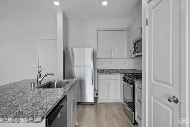 kitchen featuring sink, white cabinetry, light stone counters, stainless steel appliances, and light hardwood / wood-style floors