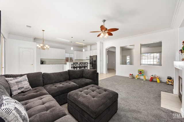 living area featuring light carpet, visible vents, arched walkways, ornamental molding, and ceiling fan with notable chandelier