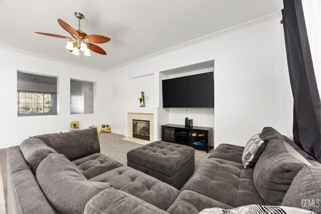 carpeted living room featuring a ceiling fan, baseboards, crown molding, and a tiled fireplace