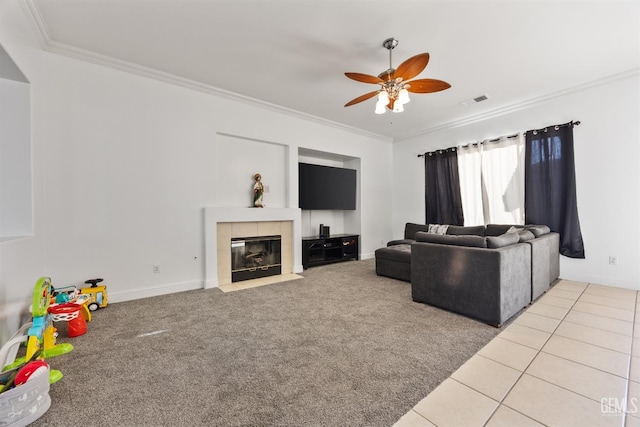 carpeted living area with ornamental molding, a tile fireplace, visible vents, and a ceiling fan