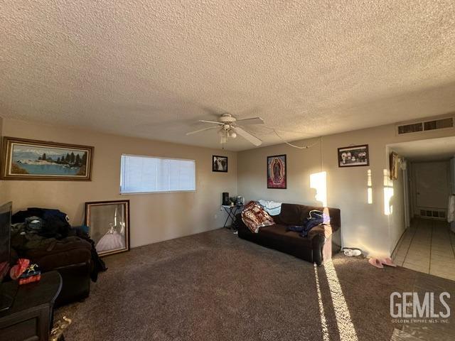 carpeted living room featuring ceiling fan and a textured ceiling