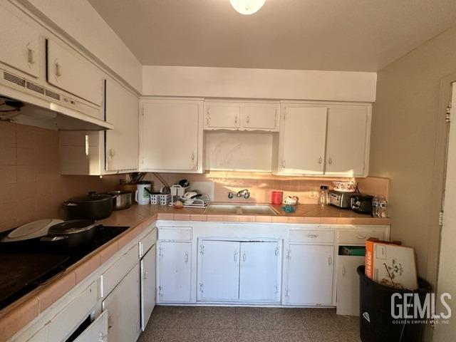 kitchen featuring tile countertops, black cooktop, sink, and white cabinets