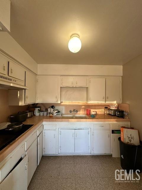 kitchen with tile countertops, white cabinetry, sink, and black cooktop