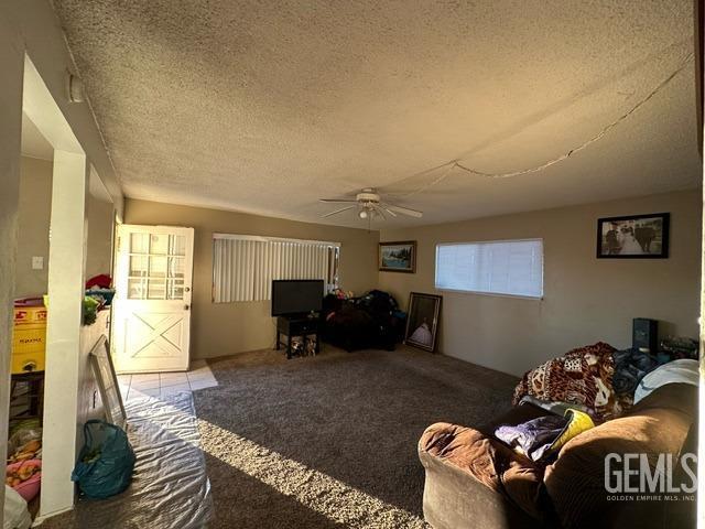 carpeted living room featuring ceiling fan and a textured ceiling