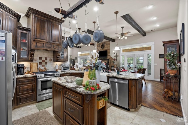 kitchen with decorative backsplash, appliances with stainless steel finishes, beamed ceiling, a kitchen island, and dark brown cabinetry