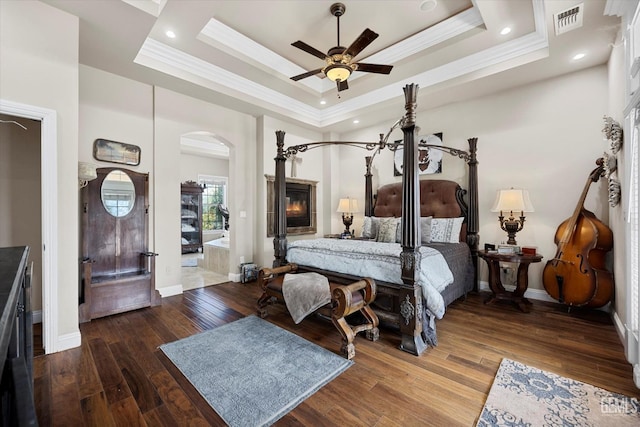 bedroom featuring ornamental molding, a tray ceiling, ceiling fan, wood-type flooring, and a fireplace