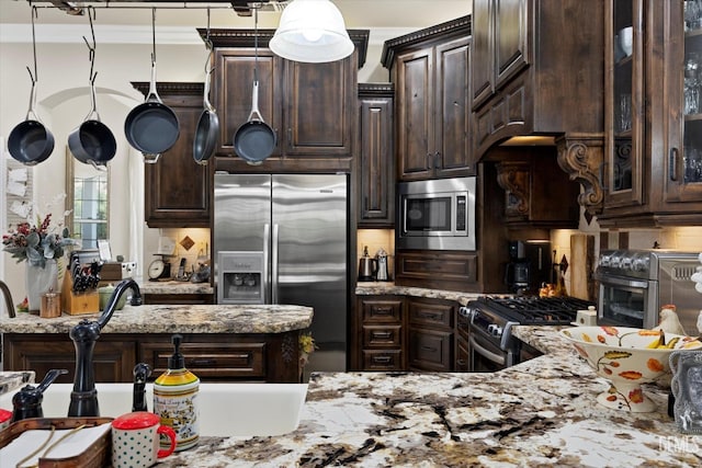 kitchen featuring dark brown cabinetry, stainless steel appliances, light stone counters, and hanging light fixtures