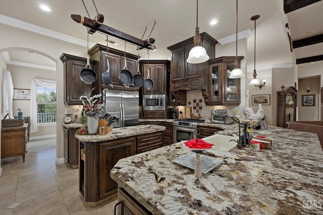 kitchen with light stone counters, decorative light fixtures, a kitchen island with sink, dark brown cabinets, and appliances with stainless steel finishes