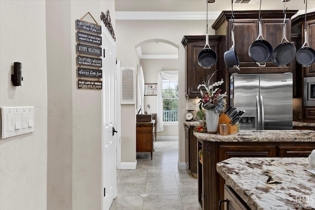 kitchen with dark brown cabinetry, stainless steel appliances, light stone counters, and ornamental molding