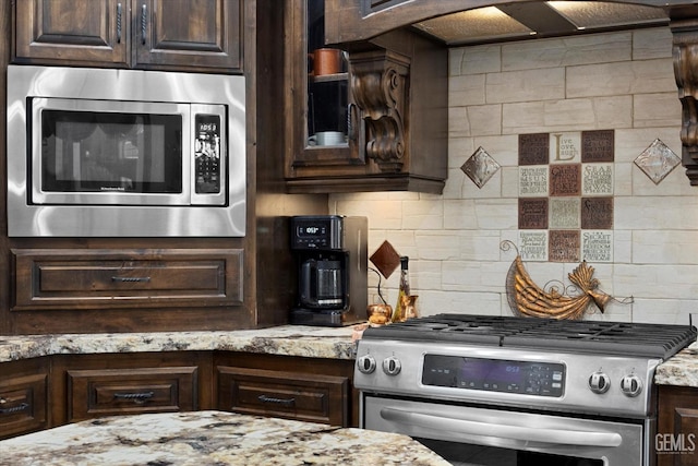 kitchen with tasteful backsplash, light stone countertops, dark brown cabinets, and appliances with stainless steel finishes