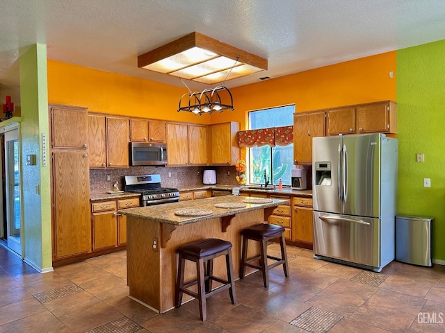 kitchen with an inviting chandelier, decorative light fixtures, appliances with stainless steel finishes, a kitchen breakfast bar, and a kitchen island