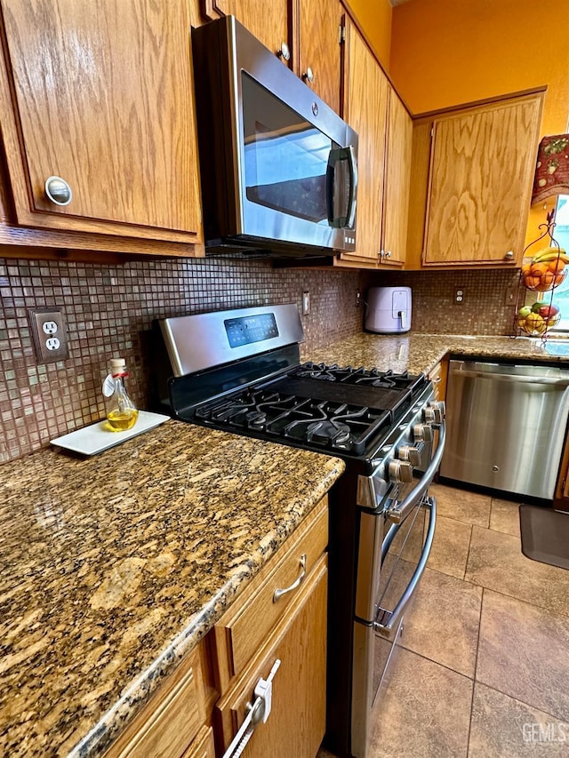 kitchen featuring stainless steel appliances, dark stone countertops, and backsplash