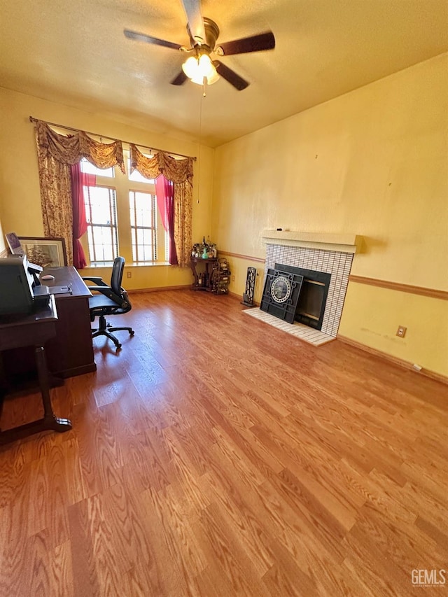 office area with a tiled fireplace, a textured ceiling, wood-type flooring, and ceiling fan