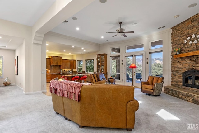 living room featuring light colored carpet, a stone fireplace, ceiling fan, and sink