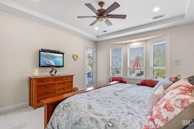 bedroom with multiple windows, access to outside, ceiling fan, and a tray ceiling