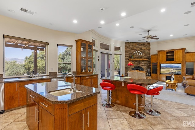 kitchen with a breakfast bar, ceiling fan, a spacious island, sink, and a stone fireplace