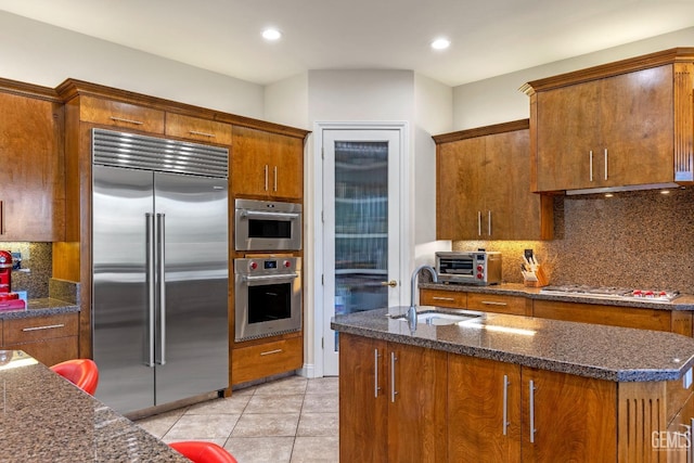 kitchen with backsplash, sink, dark stone countertops, light tile patterned flooring, and stainless steel appliances