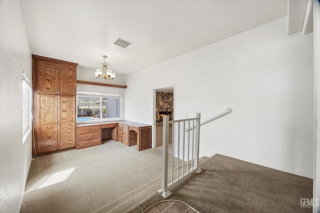 interior space featuring a stone fireplace, an inviting chandelier, built in desk, decorative light fixtures, and light colored carpet