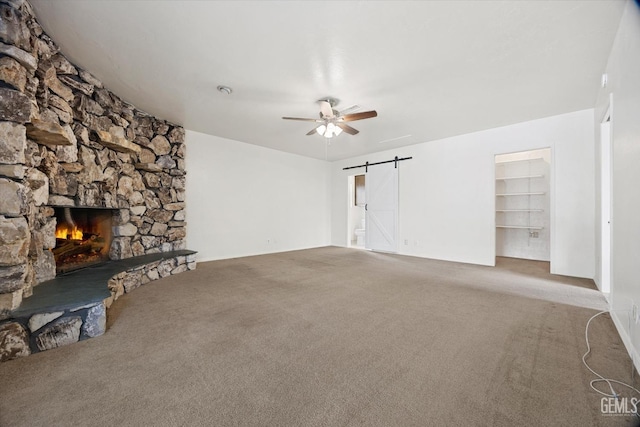 unfurnished living room featuring ceiling fan, a fireplace, a barn door, and carpet flooring