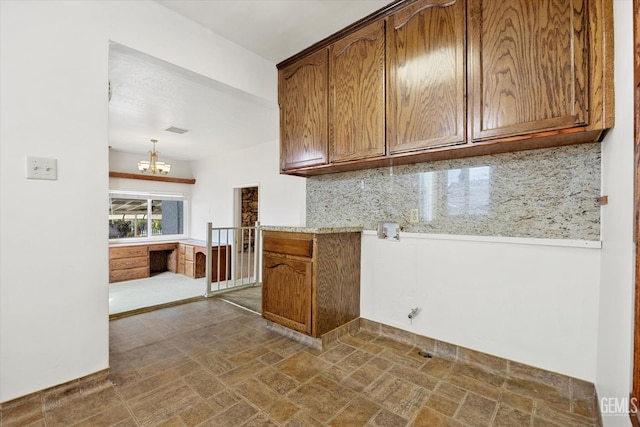 kitchen featuring pendant lighting, decorative backsplash, light stone countertops, and a chandelier