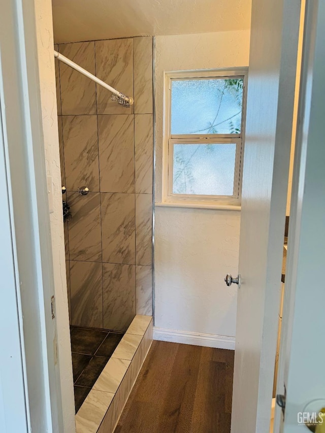 bathroom with wood finished floors, a tile shower, and baseboards