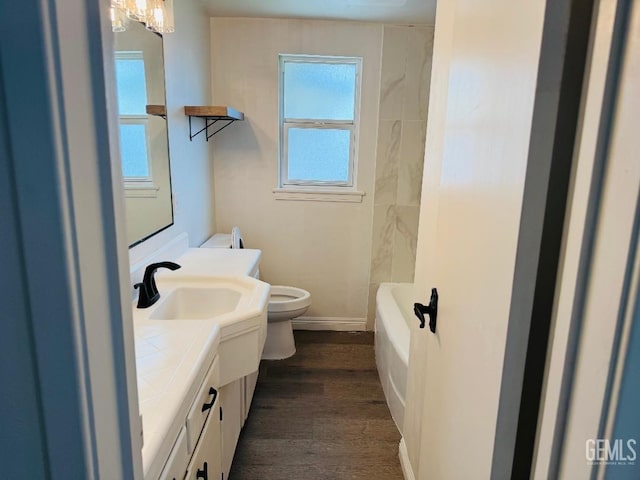 bathroom with toilet, wood finished floors, vanity, baseboards, and a bathtub