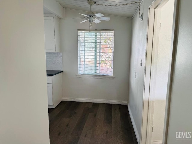 unfurnished dining area with vaulted ceiling, dark wood finished floors, baseboards, and ceiling fan