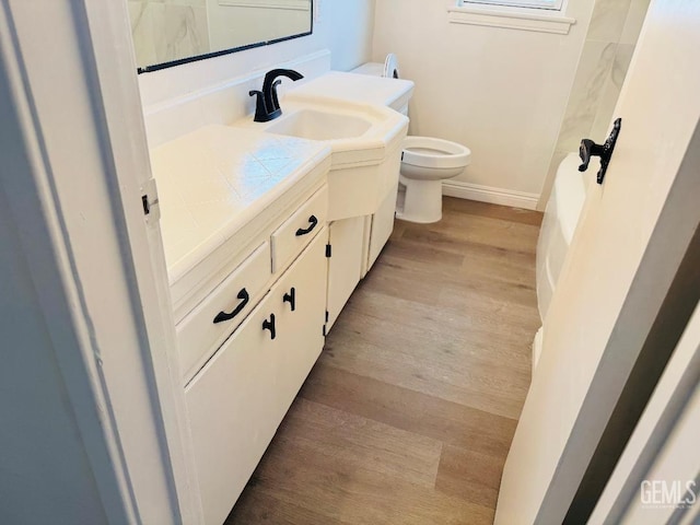 bathroom with toilet, baseboards, wood finished floors, and vanity